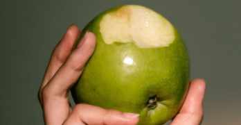 Hand holding an apple with a bite out of it.